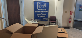 UCE of FIT banner on wall with moving cart and boxes in the foreground